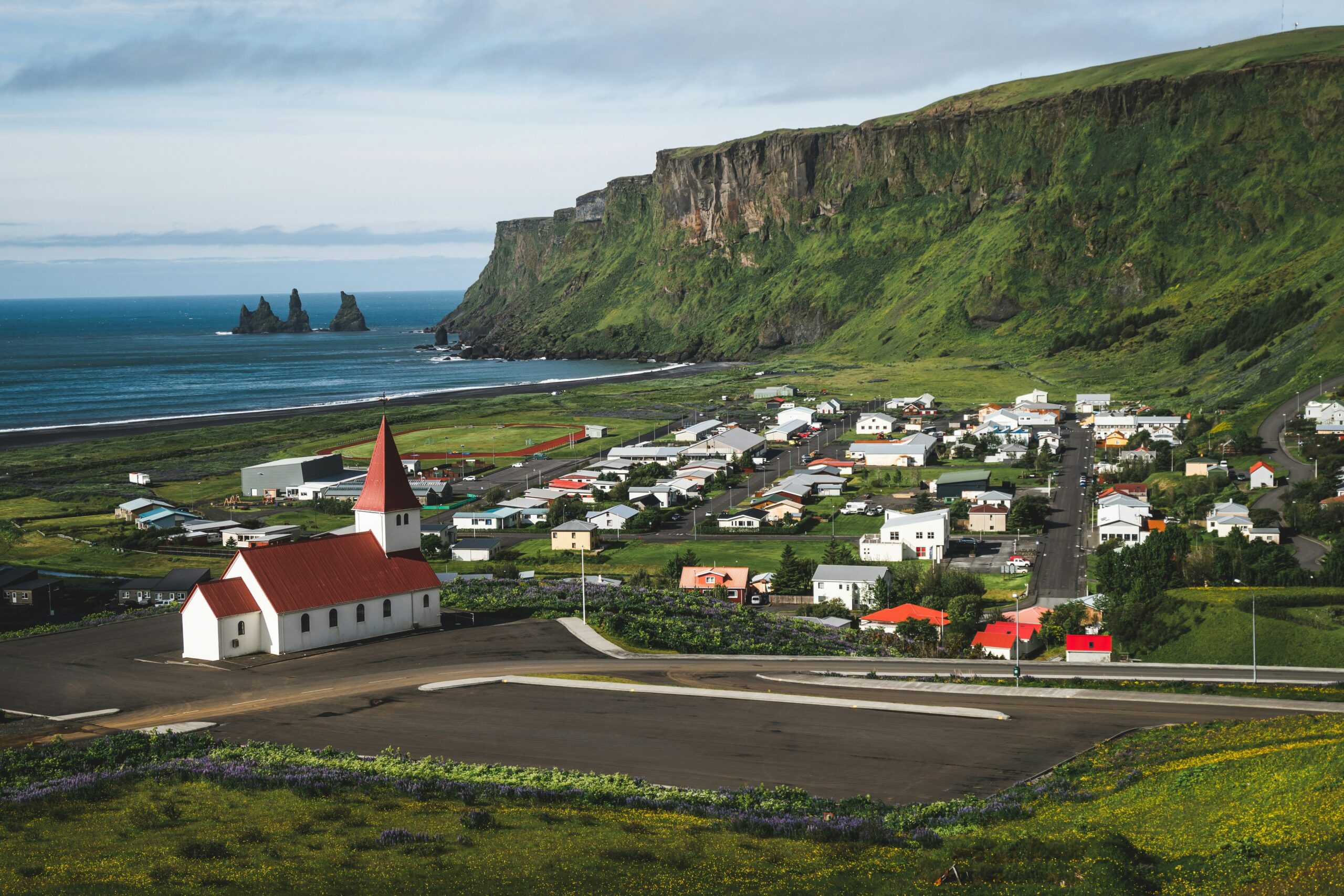 Panoramic view of Vík í Mýrdal, Iceland, with its iconic church, black sand beach, sea cliffs, and Reynisdrangar sea stacks on a guided small group adventure for solo travelers age 45+.